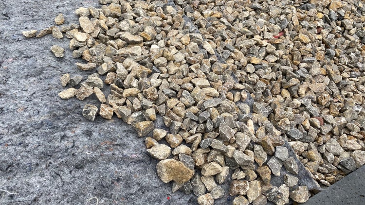 Schotter auf einem grauen Geotextilvlies für Gartenprojekte.