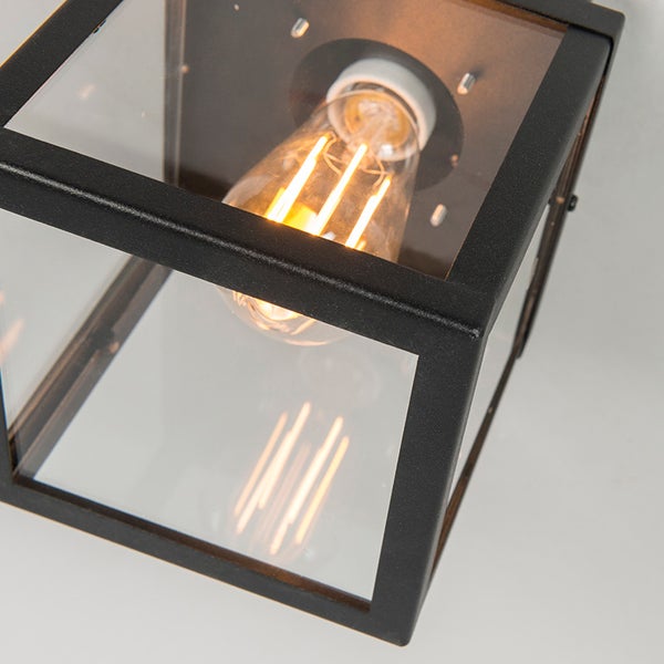 Nahaufnahme einer modernen Außenwandleuchte mit schwarzem Metallrahmen, klarem Glas und einem leuchtenden LED-Filament-Leuchtmittel.