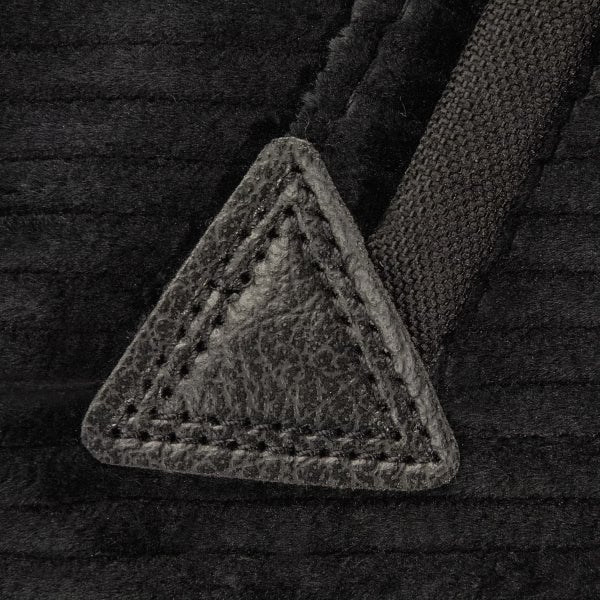 Detailaufnahme eines Kissenbezugs aus Cord mit dreieckigem Kunstleder-Patch, Ziernaht und gewebtem Band.