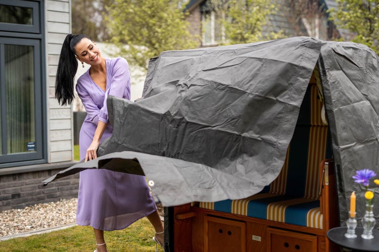 Frau deckt Strandkorb mit einer Schutzplane ab