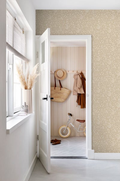 Helle, organisierte Raumszene mit floral gemusterter Tapete an der Wand, einer offenen weißen Tür und einem Flur mit Holzpaneelen und Kinderlaufrad.