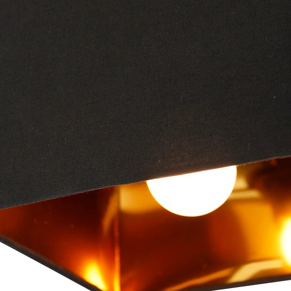 Nahaufnahme eines Lampenschirms mit schwarzem Stoff außen und goldfarbener reflektierender Innenseite sowie einem leuchtenden Leuchtmittel.