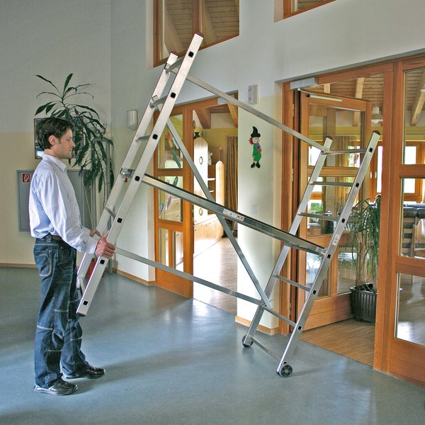 Mann transportiert eine fahrbare Arbeitsbühne aus Aluminium.