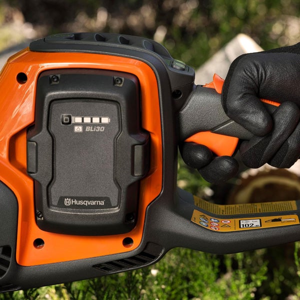Husqvarna Akku Kettensäge mit eingesetztem BLi30 Akku und Hand in Arbeitshandschuh am Bediengriff