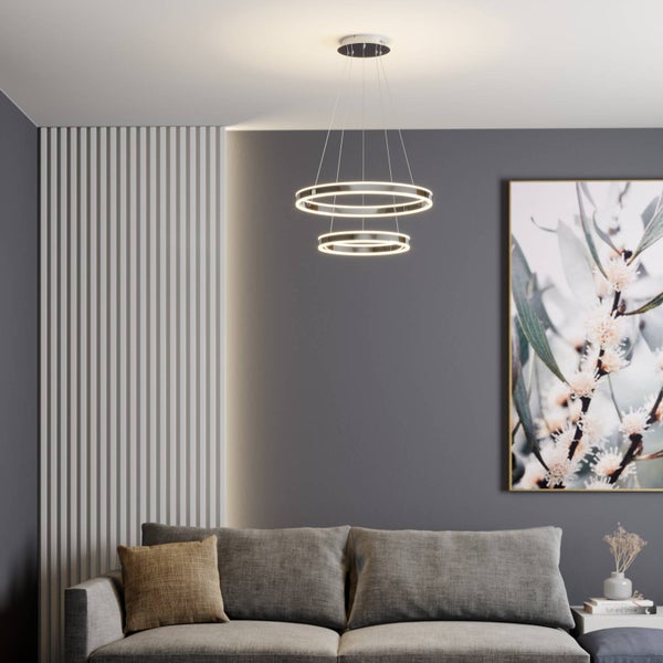 Moderne LED-Pendelleuchte mit drei Ringen in einem hellen, organisierten Wohnzimmer mit grauem Sofa und weißer Lamellenwand.