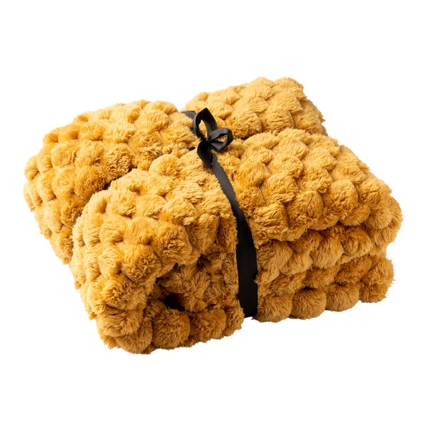 Weiche, ockergelbe Kuscheldecke mit Noppenstruktur, zusammengebunden mit schwarzem Band.