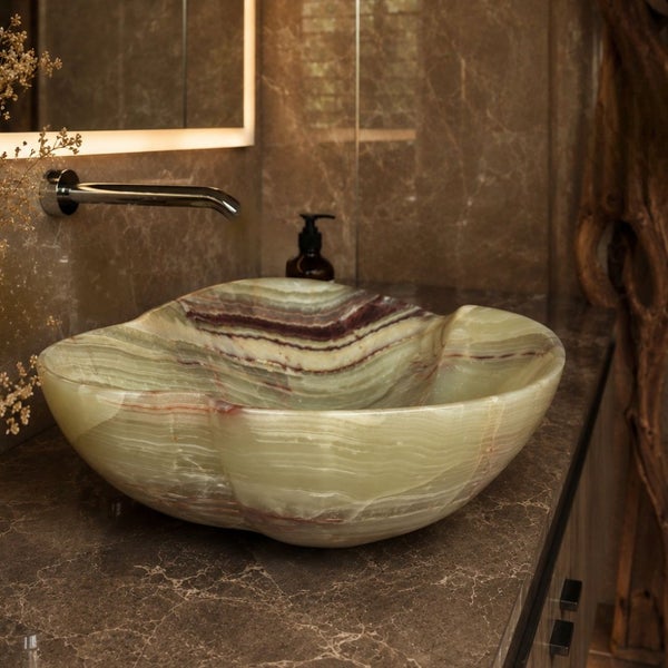 Aufsatzwaschbecken aus Naturstein Onyx in organischer Form auf einer Marmorplatte im Badezimmer mit Unterputzarmatur und beleuchtetem Spiegel.