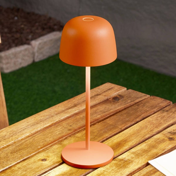 Moderne orangefarbene LED-Akku-Tischleuchte für den Außenbereich auf einem Holztisch stehend.