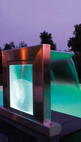 Moderner Pool-Wasserfall aus Edelstahl mit integrierter LED-Beleuchtung an einem Schwimmbecken bei Dämmerung.