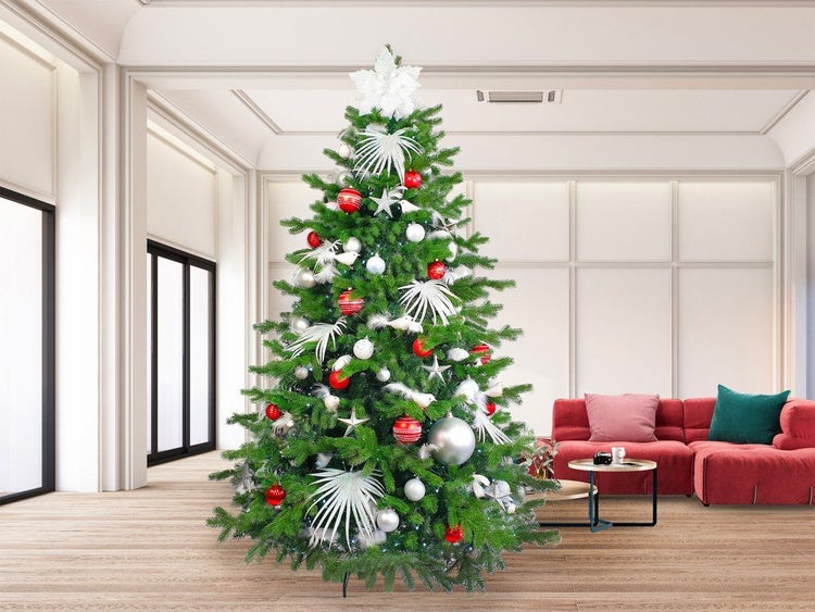 Geschmückter künstlicher Weihnachtsbaum in einem hellen Wohnzimmer mit rotem Sofa und weihnachtlicher Dekoration in Rot und Silber.