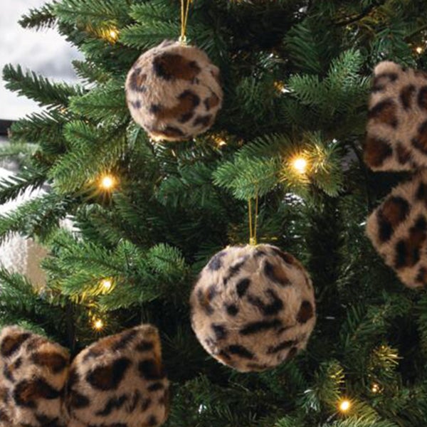 Weihnachtskugeln mit Kunstfell in Leopardenmuster hängen an einem geschmückten Weihnachtsbaum mit Lichterkette.