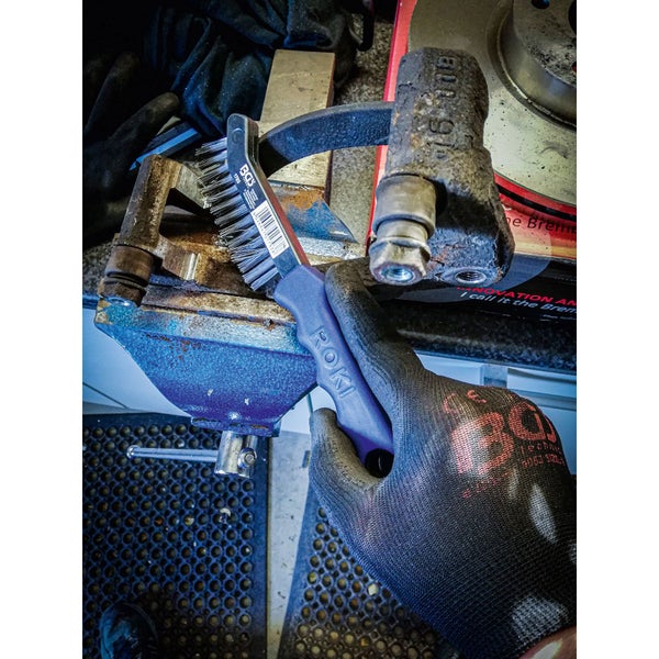 Eine Person reinigt mit einer Drahtbürste ein Werkstück, das in einen Schraubstock eingespannt ist.