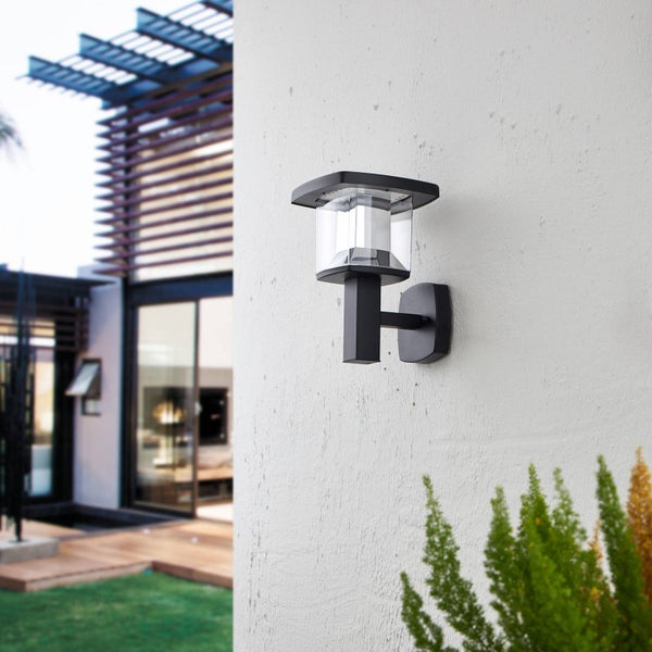 Moderne schwarze LED Außenwandleuchte aus Metall mit klarem Gehäuse, montiert an einer weißen Hauswand neben einer Terrasse.