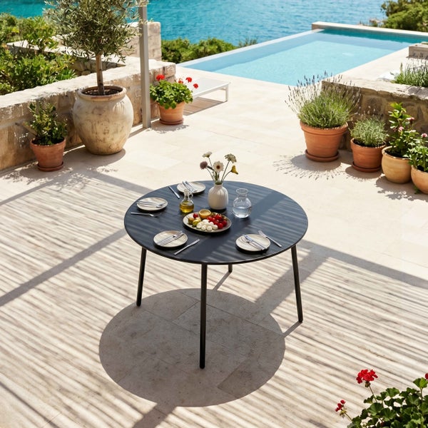 Moderner runder Gartentisch aus Metall auf einer hellen Steinterrasse neben einem Pool, gedeckt für vier Personen mit Snacks und Dekoration.