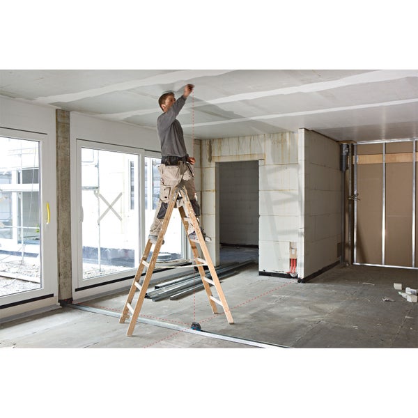 Mann auf einer Leiter, der mit einem Lasergerät in einem Rohbau eine Decke vermisst.