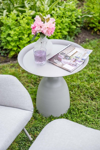 Runder grauer Beistelltisch aus Metall mit Sockel in einem Garten, dekoriert mit Vase, Blumen, Glas und Magazin.