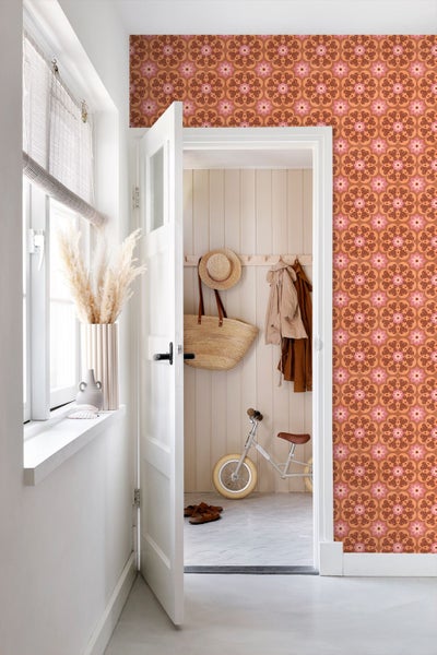 Innenraum mit gemusterter Tapete im floralen Mandala-Design. Blick durch eine weiße Tür in einen Flur mit Holzpaneelen und einem Laufrad.