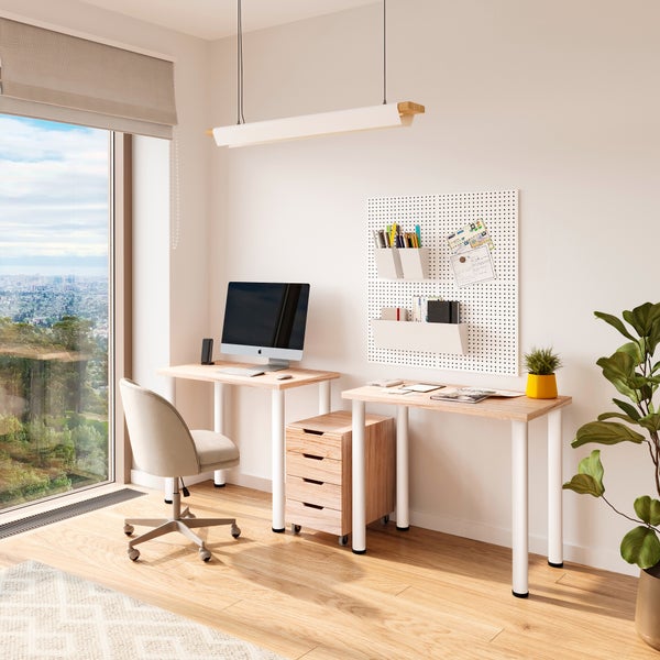 Ein moderner, heller Arbeitsplatz mit zwei Schreibtischen, Rollcontainer, ergonomischem Stuhl, Wandlochplatte und Pendelleuchte in einem Raum.
