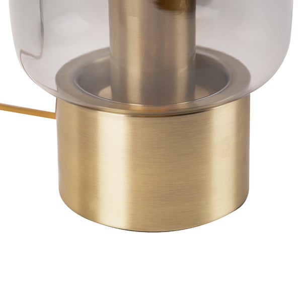 Detailansicht einer Tischleuchte mit einem zylindrischen Sockel aus gebürstetem Metall und einem Schirm aus klarem Glas.