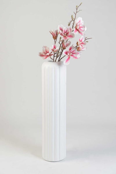 Weiße hohe Vase mit Rillenstruktur und künstlichen Magnolienzweigen mit rosa-weißen Blüten.