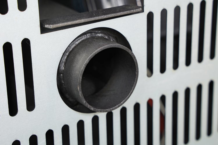Detailansicht des Rauchrohranschlusses an der Metallrückwand eines Kaminofens mit Lüftungsschlitzen