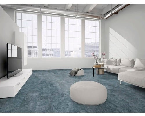 Moderner, heller Wohnraum mit Sofa, großen Fenstern und blau-grauem Bodenbelag in Steinoptik.