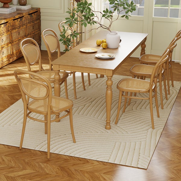 Esszimmergarnitur mit rechteckigem Holztisch und sechs Stühlen mit Wiener Geflecht auf einem gemusterten Teppich in hellem Ambiente.