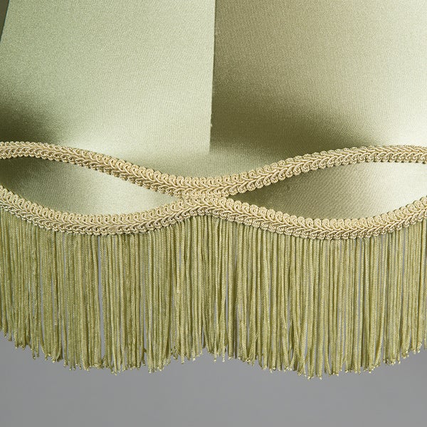 Grüner Lampenschirm aus glänzendem Stoff mit dekorativer Borte und hängenden Fransen.
