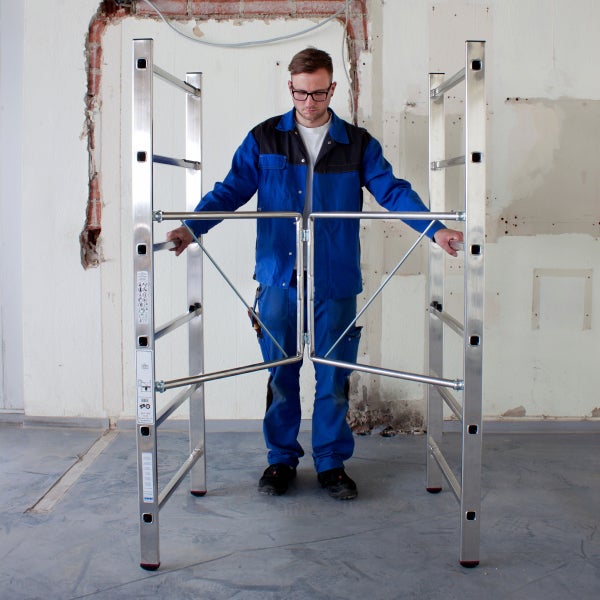 Mann montiert ein Klappgerüst aus Aluminium vor einer unfertigen Wand.