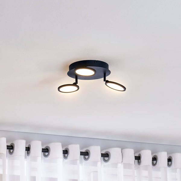 Moderne LED-Deckenleuchte in Schwarz mit drei runden, schwenkbaren Lichtelementen montiert an der Decke über einem Vorhang.