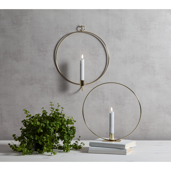 Zwei runde Kerzenhalter aus Metall mit weißen Kerzen, dazu eine Zimmerpflanze und Bücher.