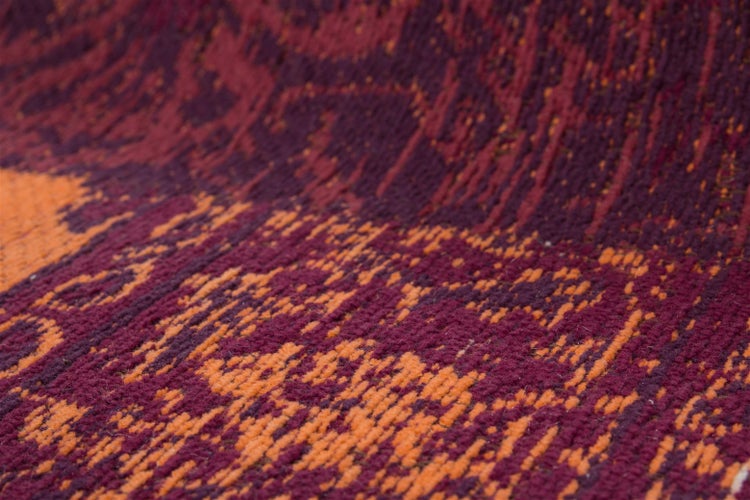 Detailaufnahme eines gewebten Teppichs in Rot- und Orangetönen mit abstraktem Muster und strukturierter Oberfläche.