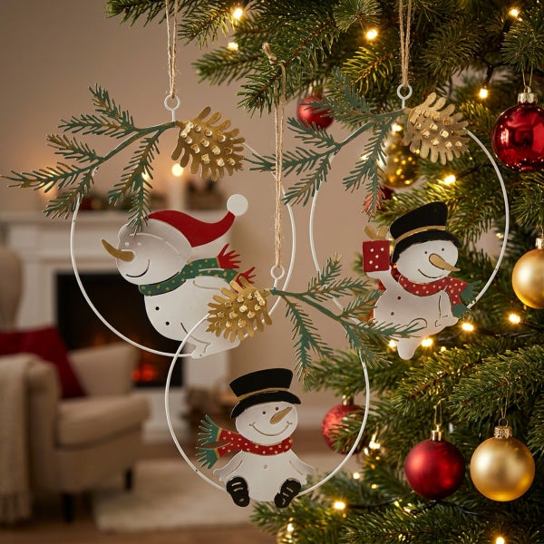 Drei runde Weihnachtsanhänger aus Metall mit Schneemann Motiven und Tannenzweigen, hängend an einem Weihnachtsbaum