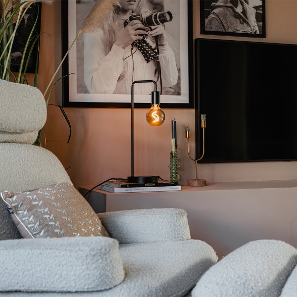 Dekorative Szene mit Lampe, Kerzen und Sessel in einem Wohnraum.