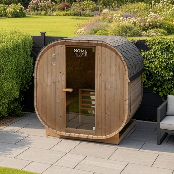 Fasssauna aus Holz mit Glasfront im Garten platziert, Home Deluxe Logo auf der Glastür, moderne Sauna für den Außenbereich auf Terrassenplatten