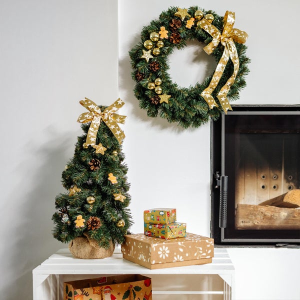 Weihnachtlicher Tischschmuck mit einem grünen Kranz, einer weißen Kerze, Tannenzapfen und goldenen Kugeln auf einem Holztisch.