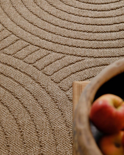 Gewebter Teppich mit strukturiertem Muster aus Bögen und Linien in Beige.