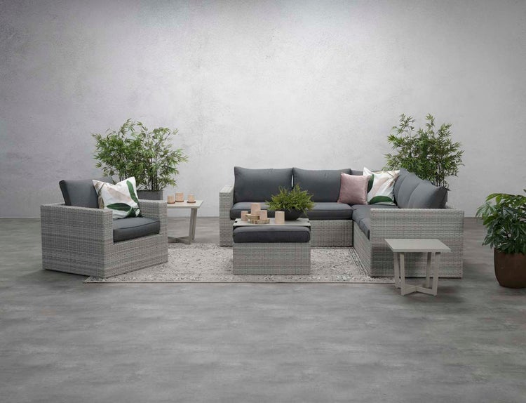 Modernes Garten-Lounge-Set aus grauem Polyrattan, bestehend aus Ecksofa, Sessel, Hocker und Beistelltischen, dekoriert mit Pflanzen auf einem Teppich.
