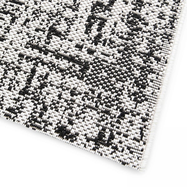 Gewebter Teppich mit schwarz-weißem Muster und eingefasstem Rand.