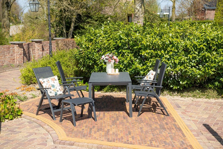Gartenmöbel-Set aus anthrazitfarbenem Metall auf einer gepflasterten Terrasse, bestehend aus einem quadratischen Tisch, vier Klappstühlen und einem Hocker.