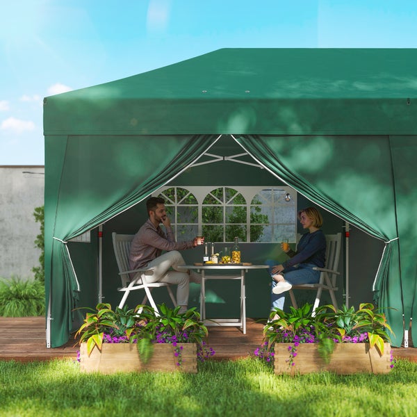 Grüner Gartenpavillon mit Seitenwänden und Fenstern, zwei Personen sitzen an einem Tisch auf einer Holzterrasse im Garten.