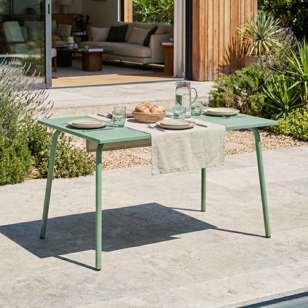 Gedeckter Gartentisch aus Metall auf einer hellen Steinterrasse vor einem modernen Wohnhaus mit Blick in den Garten.