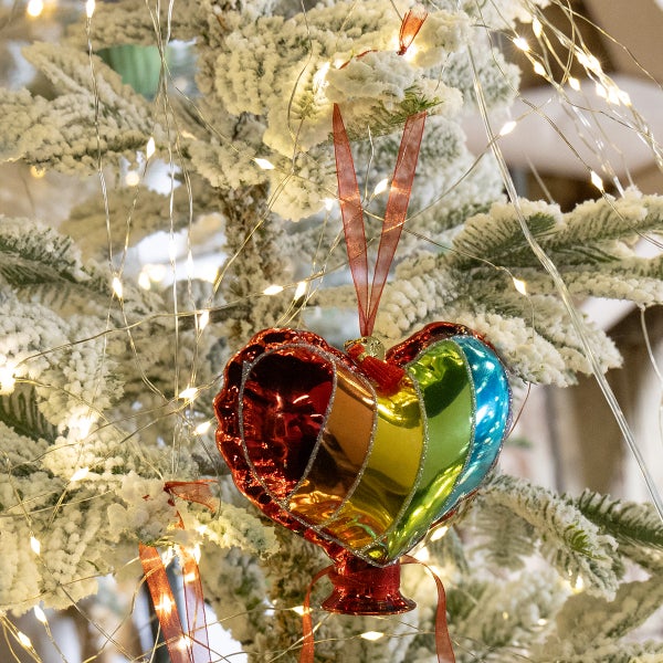 Herzförmiger Christbaumschmuck mit Regenbogenfarben an einem schneebedeckten Weihnachtsbaum