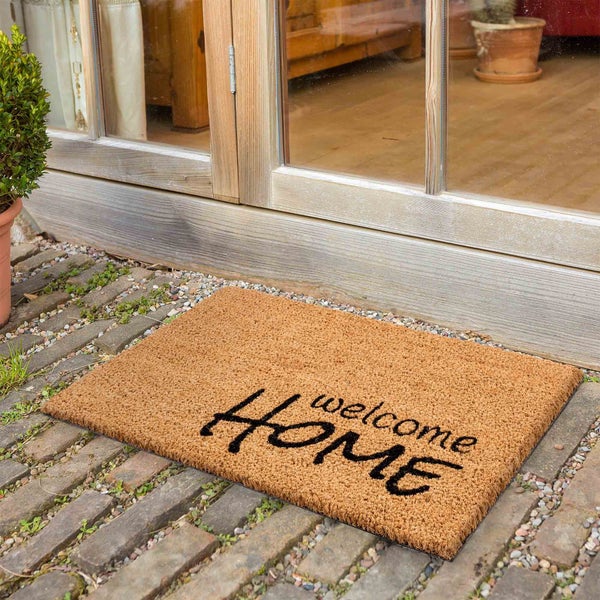 Fußmatte mit Willkommensgruß vor einer Haustür