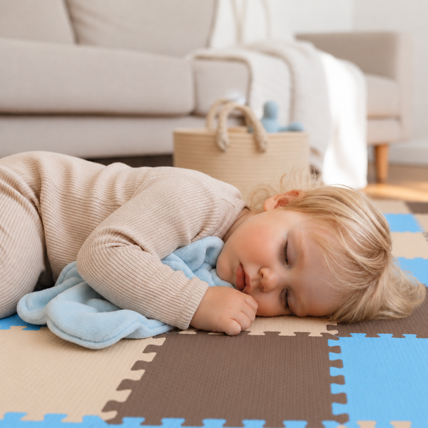 Kleinkind schläft friedlich auf einer bunten Puzzlematte aus Schaumstoff im Wohnzimmer