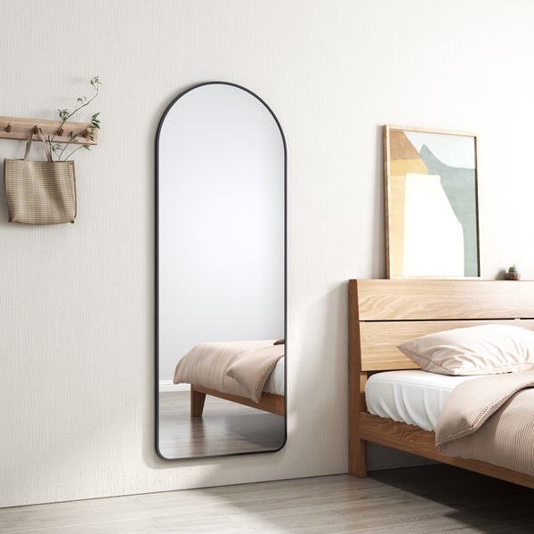 Heller Schlafraum mit einem großen wandmontierten Bogenspiegel mit schwarzem Metallrahmen neben einem Bett aus Holz.