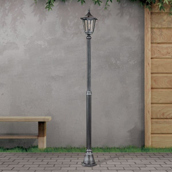 Klassische Mastleuchte aus Metall für den Garten im Außenbereich mit Mauer, Holzelementen und Bodenpflaster.