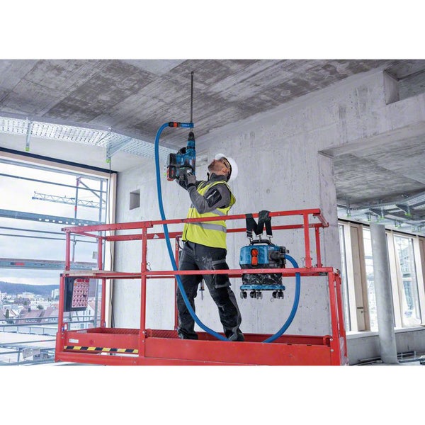 Handwerker bohrt mit einer Bohrmaschine ein Loch in die Decke, während ein Staubsauger den Bohrstaub absaugt.