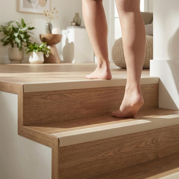 Treppenkantenprofil auf Holzoptik Treppenstufen montiert, ein Mensch steigt barfuß die Treppe in einem hellen Wohnraum hinauf.