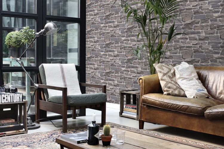 Wohnzimmer mit Sessel, Ledersofa und Steinwandtapete.
